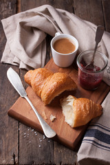 Closeup of croissant with jam and coffee on a wooden background.