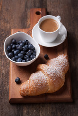roissant with coffee and blackberries on a wooden board. Selective focus