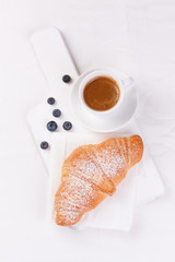 Croissant with coffee and blackberries on a white board. top view