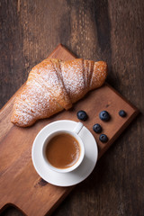 Croissant with coffee and blackberries on a wooden board. Selective focus.