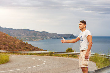  hitchhiker young man, hitchhiking on a rural road hitchhiking on the background of the road, blue see and sky 