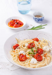 .Italian spaghetti pasta with baked cherry tomatoes, mozzarella and spring onions in a white bowl on a white table.