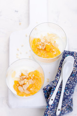 Sweet peach and pear compote with yogurt in a glass and jam on a white board.