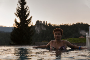 White tanned woman in outdoor swimming pool at sunset.