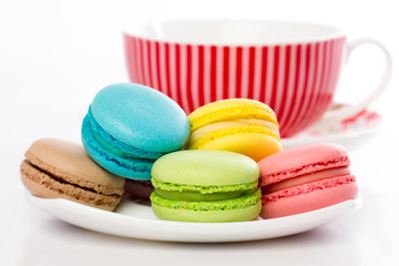 Collection of brightly colored French macarons on white background, lying in a saucer, standing next to the kettle