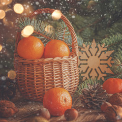 Obraz na płótnie Canvas Basket with tangerines, cones, nuts and fir branches on wooden b