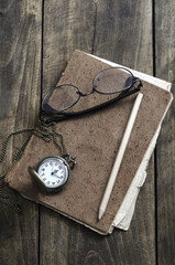 Pocket watch, glasses and old notebook on table