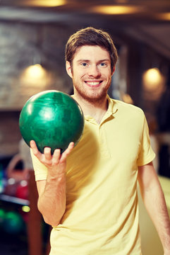 happy young man holding ball in bowling club