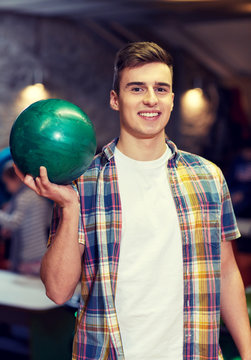 happy young man holding ball in bowling club