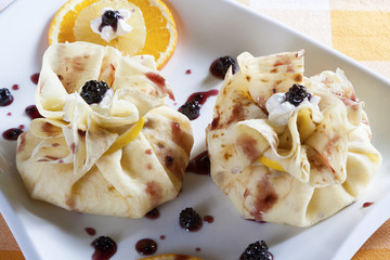 Two crepes, wrapped as bags, with sweet filling served on a white plate with  blackberries, orange,...
