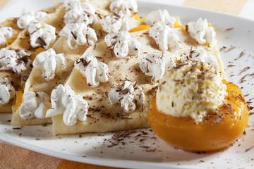 Pancakes stuffed with vanilla cream and peach, decorated with whipped cream and grated chocolate, served on a white plate.