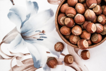 Top View of Hazelnuts in Wooden Bowl on a Napkin with Flower Des