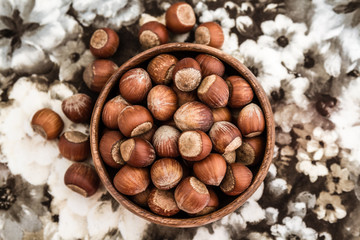 Top View of Hazelnuts in Wooden Bowl on a Napkin with Flower Des