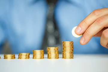 Male hand stacking gold coins into increasing columns