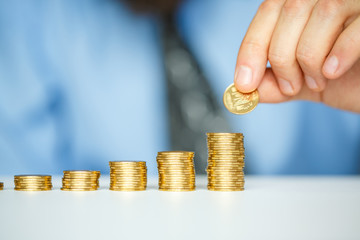 Male hand stacking gold coins into increasing columns