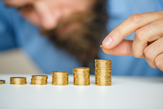 Beared man stacking gold coins into increasing columns