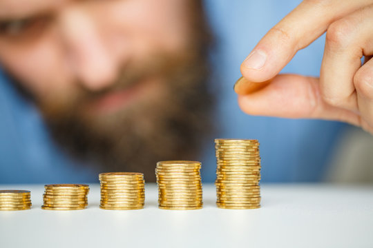 Beared man stacking gold coins into increasing columns