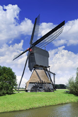 Fototapeta na wymiar Ancient wooden drainage windmill in a green polder with a blue sky and dramatic clouds.