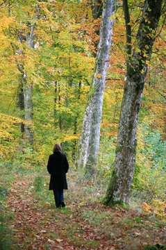 Woman with black coat walking in a forest.