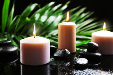 Obraz na płótnie Canvas Aroma candles and pebbles with palm leaves on dark background