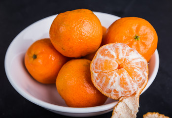 Organic mandarin oranges in white bowl on black table