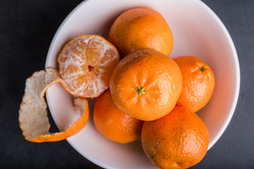 Organic mandarin oranges in white bowl on black table