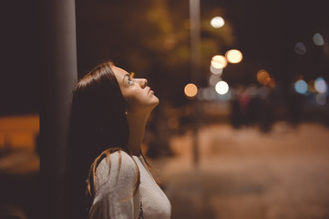 Sad young lady thinking about something leaning against street lamp