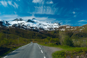 Car on the asphalt road to Norvegian mountains in sunny clear da