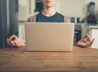Young woman meditating by laptop