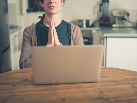 Woman praying by laptop in kitchen