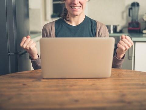 Young woman with laptop fist pumping in kitchen