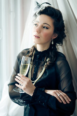 Portrait of beautiful woman in black dress and glass of champagne and looking out the window