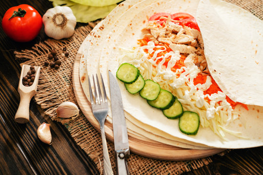 
shaverma , roll, pita bread with fried chicken, cabbage , tomatoes, cucumbers , carrots , garlic , mayonnaise and spices on a wooden background