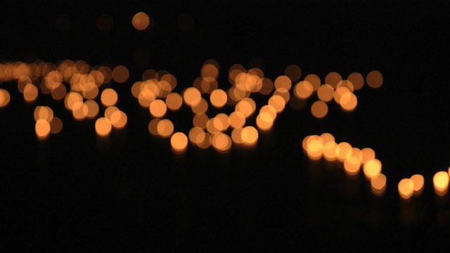 Burning candles float on water during Loi Khrathong celebration in Sukhothai, Thailand. Deep out of focus.