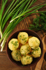 Boiled potatoes with greens in bowl on table close up