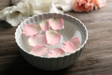 Tender pink rose petals in a bowl of water on wooden background