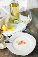 Served wooden table with tasty salmon cream soup, wine and lemon on it, close up