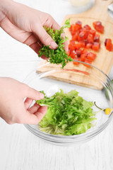 Female hands adding lettuce leaves into bowl with salad, close-up