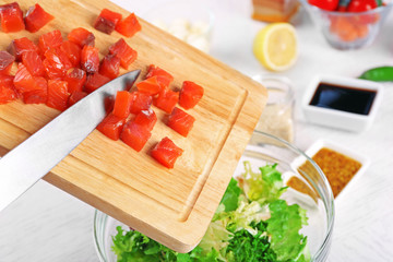 Female hands adding pieces of salmon into bowl with salad, close-up