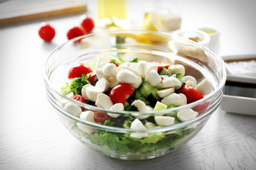 Tasty salad in glass dish on color wooden table background