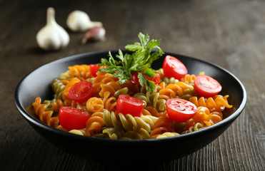 Delicious macaroni dish in black bowl on served wooden table