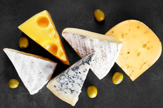 Different kinds of cheese, olives and rosemary on grey background, close up