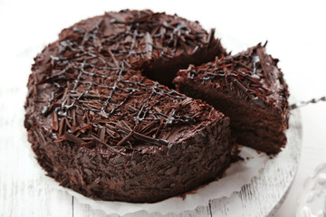 Sliced chocolate cake on wooden table, on light background