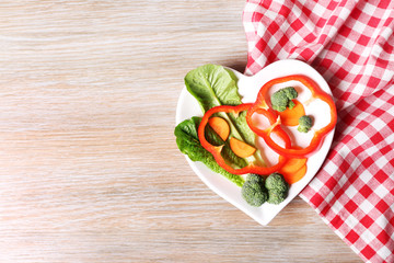 Useful cut vegetables on a plate in the form of heart on wooden table top view