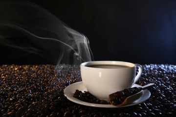 Cup of hot coffee among coffee beans on dark background