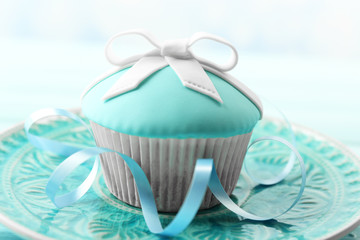 Tasty cupcake with bow on color wooden table, on bright background