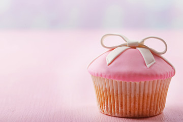 Tasty cupcake with bow on color wooden background
