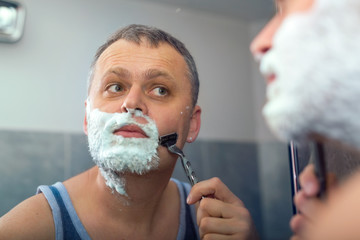 Mature handsome man shaving in front of mirror