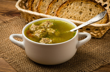 Soup with meatballs in a white bowl on the wooden background.