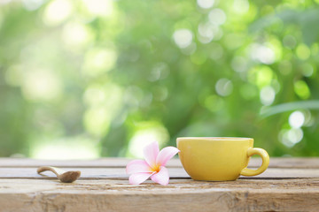 yellow coffee cup with flower and wooden spoon on wooden table